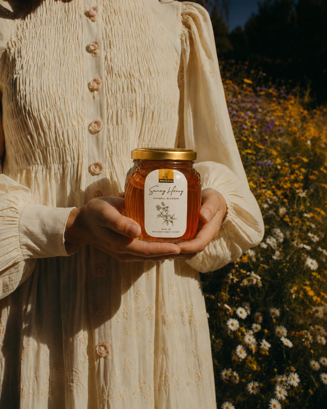 Банка Sunny Honey в руках на фоне льняного платья и цветущего луга